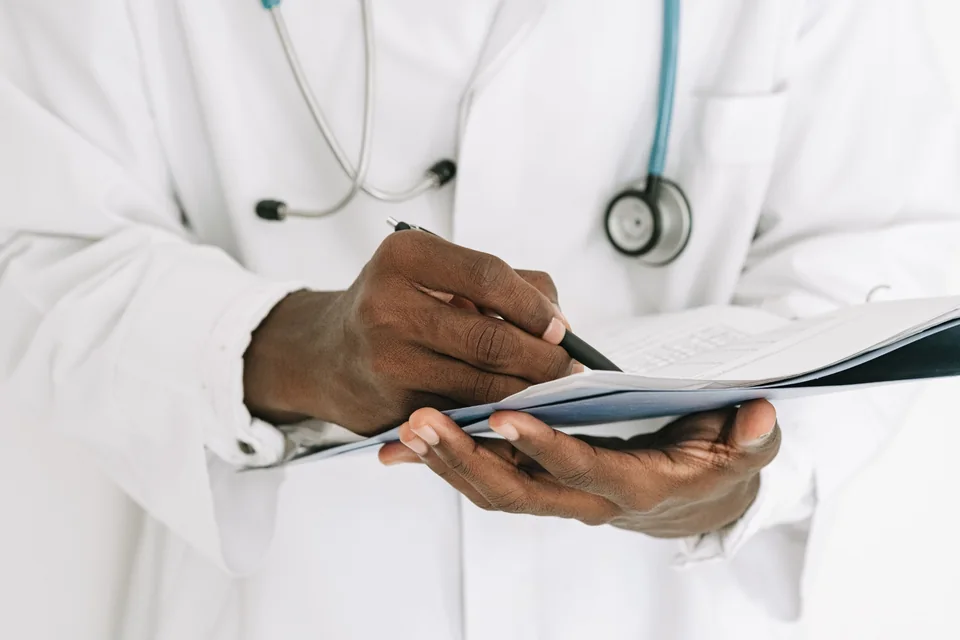 Close-up of a person in a white coat writing on a clipboard.